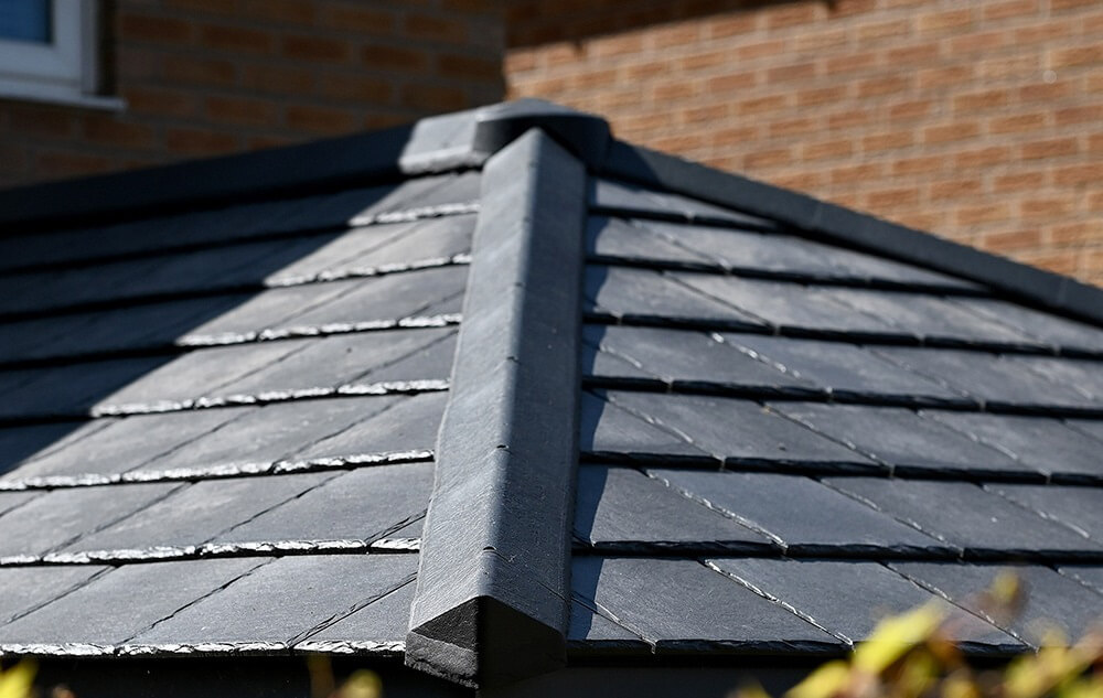 Exterior view of a house with an Equinox solid roof conservatory extension. The conservatory showcases a contemporary design with a slate-gray tiled pitched roof that harmonizes with the brick exterior of the home.