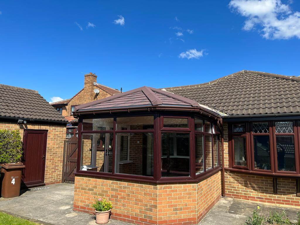 Tiled roof conservatory next to brown uPVC bow window